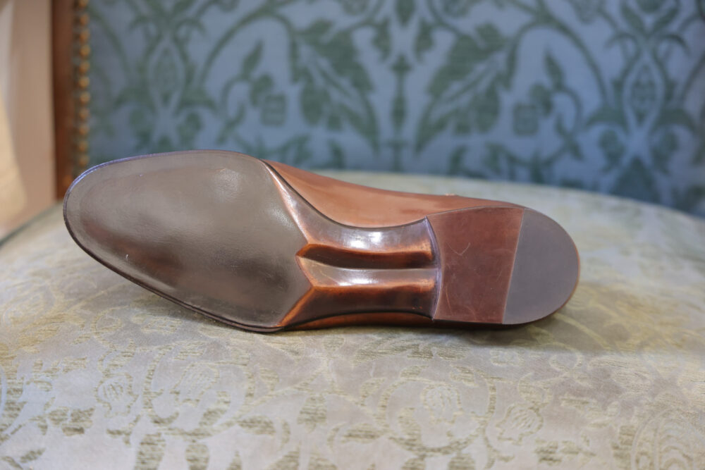 A close-up of the smooth, polished sole of a brown leather shoe.