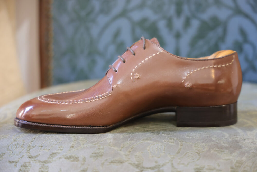 A polished brown leather shoe with decorative stitching and a low heel.