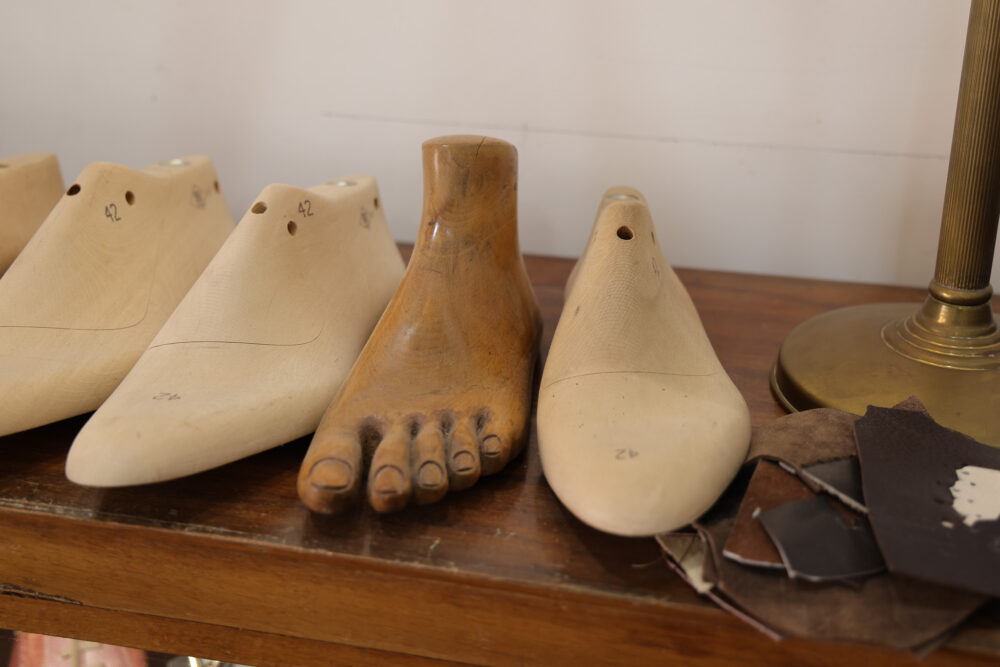Wooden shoe lasts in various shapes, including a detailed foot mold, displayed on a wooden surface.