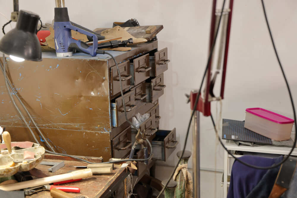 A blue electric tool is resting on a worn brown cabinet with multiple drawers in a shoemaker's workshop.