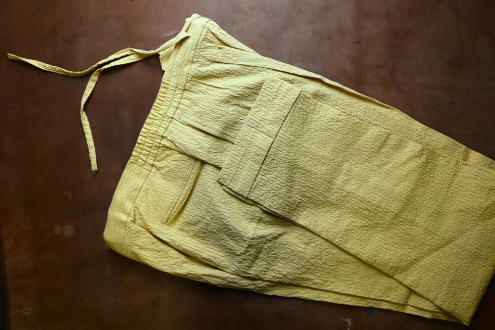 A pair of textured yellow pants with a drawstring waist and a side pocket.