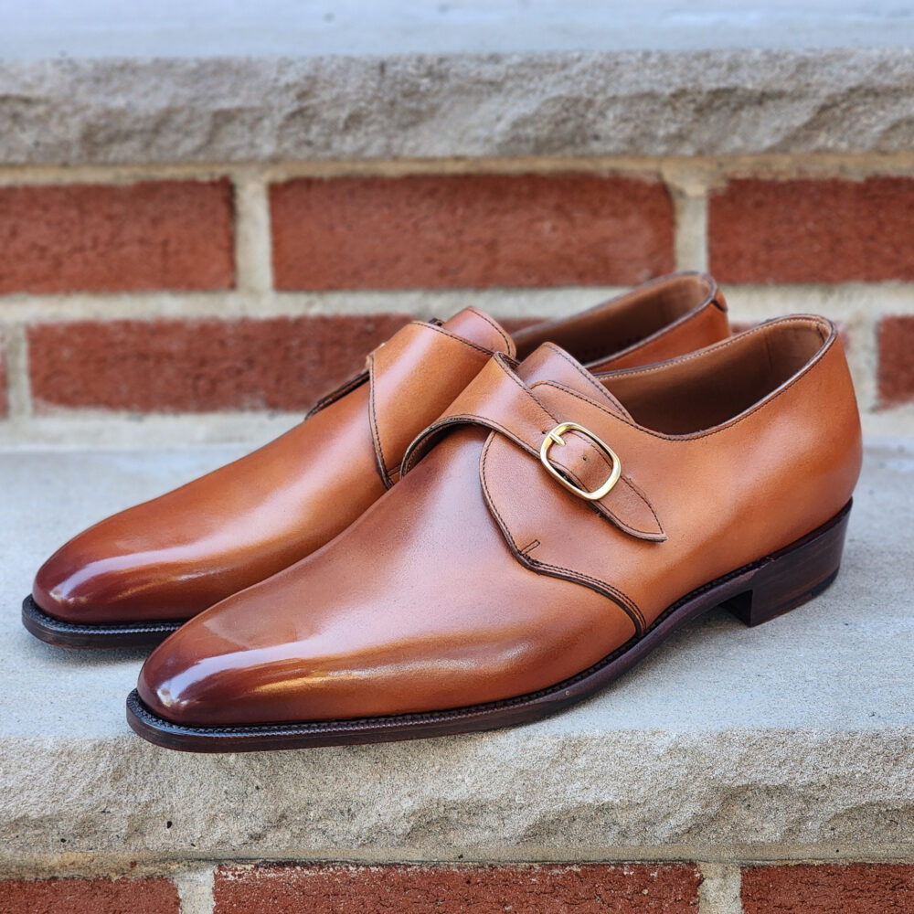 A pair of polished tan leather shoes with a side buckle detail.