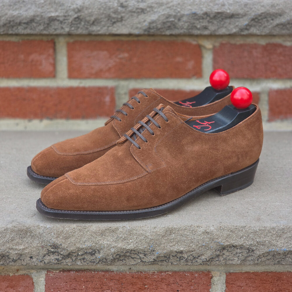 A pair of brown suede shoes with red shoe trees.