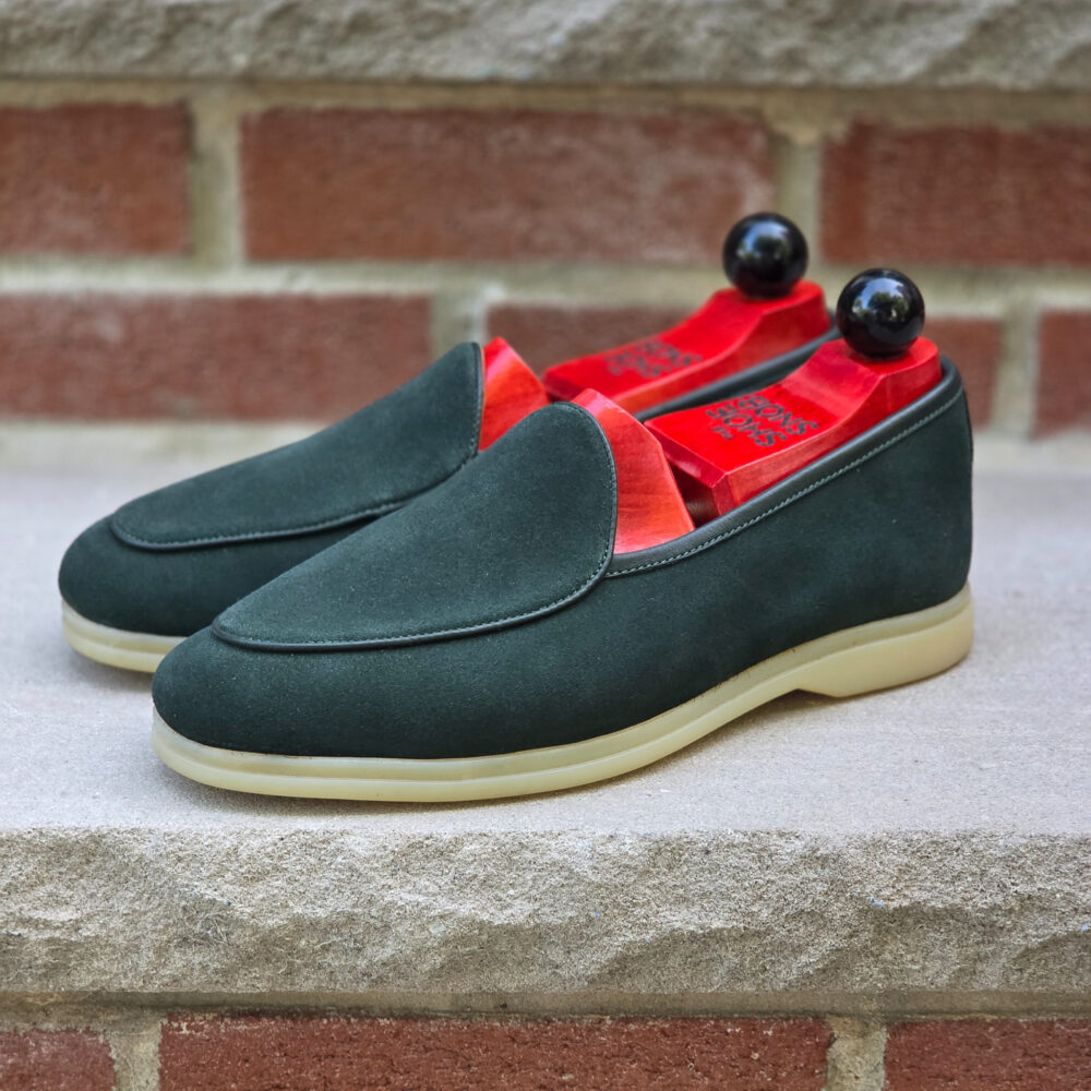 A pair of dark green suede loafers with a beige sole and red insoles.