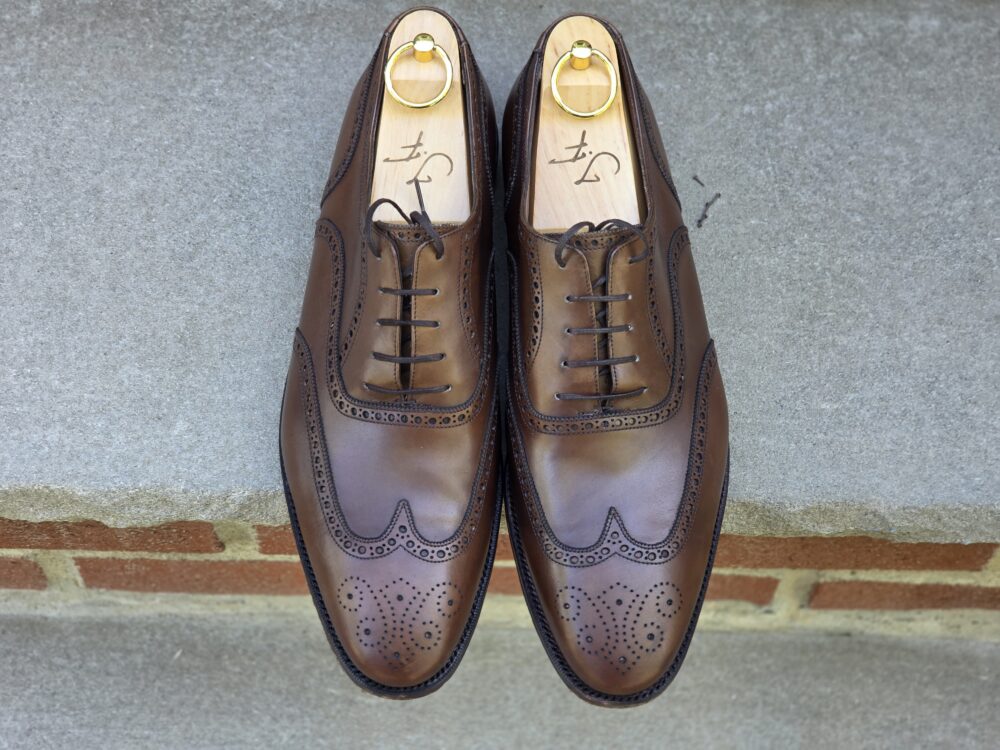 A pair of brown leather dress shoes with decorative perforations and a wooden shoe tree.