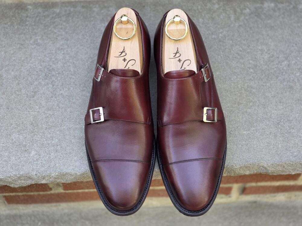 Two burgundy leather double monk strap shoes with silver buckles and wooden shoe trees visible inside.