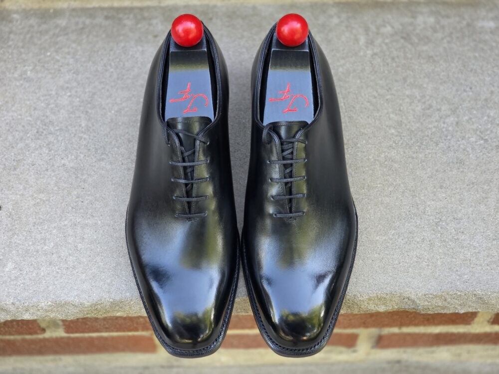 A pair of black leather dress shoes with a shiny finish and red accents on the heel.
