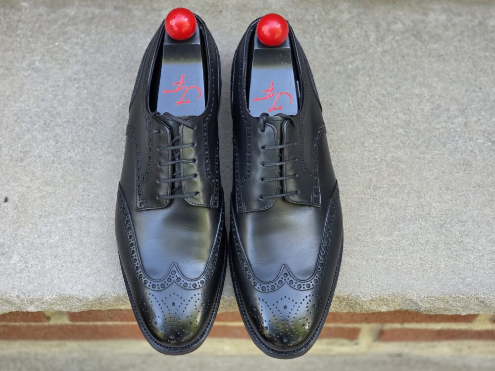 A pair of black leather dress shoes with decorative perforations and red shoehorns.