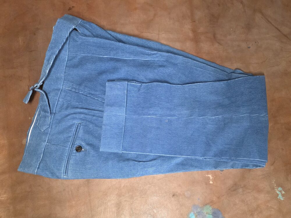 A pair of folded blue corduroy pants with a single button detail.