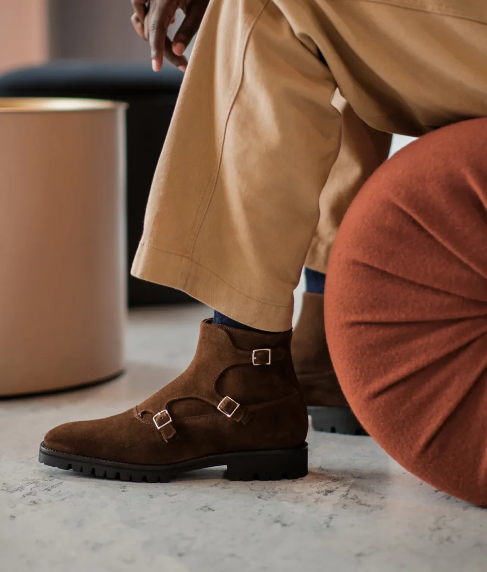 A close-up of a man's brown suede ankle boots with buckle details, featured in the Septieme Largeur Summer Sale 2026.