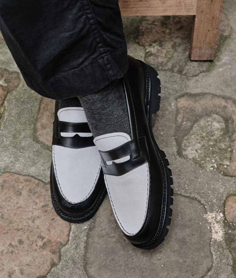 A close-up of stylish black and gray loafers worn with gray socks, featured in the Septieme Largeur Summer Sale 2026.