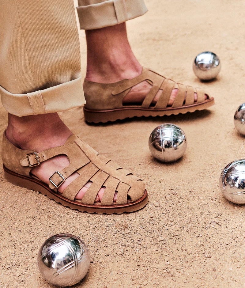 A close-up of tan suede sandals with straps, showcased for the Septieme Largeur Summer Sale 2026, surrounded by metallic balls.