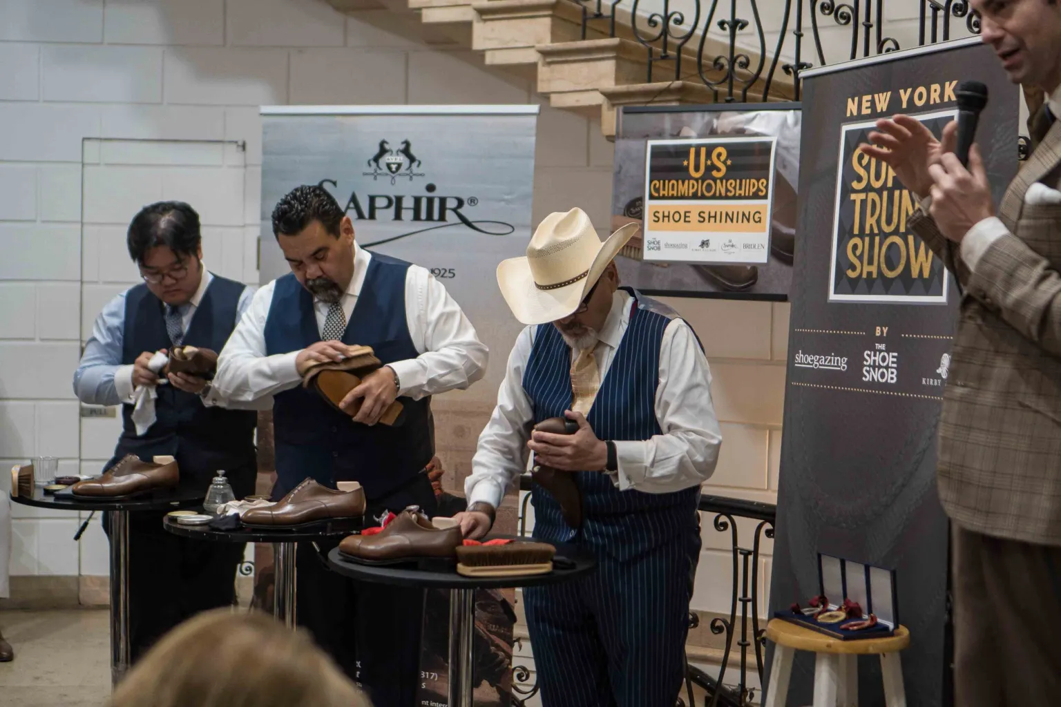 Three men in vests are polishing shoes during the Americas Shoe Shining Championships qualification event.