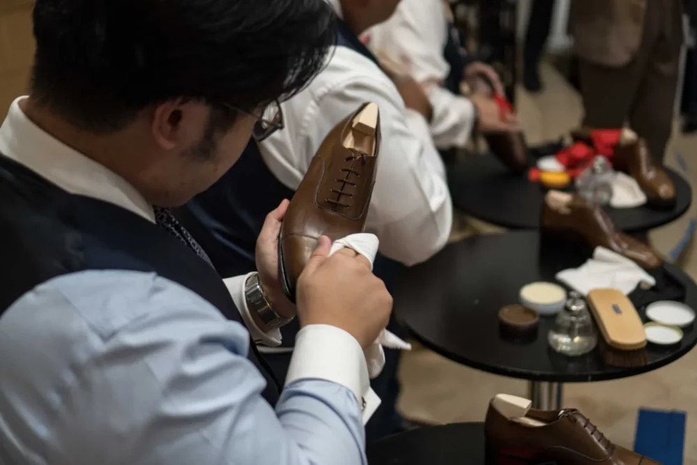A person in a vest is polishing a brown leather shoe while preparing for the Americas Shoe Shining Championships.