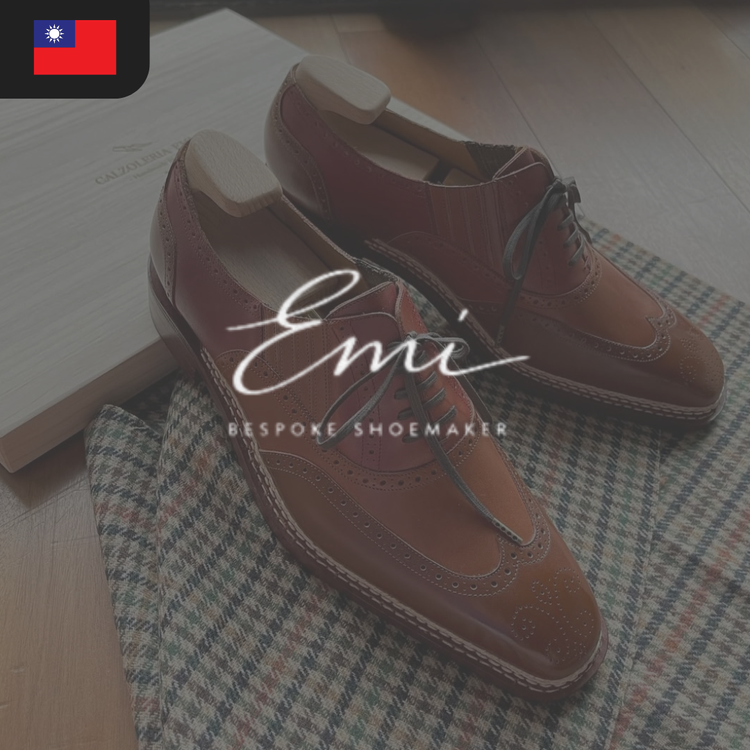 A pair of brown leather wingtip shoes with brogue detailing, placed on a patterned fabric.