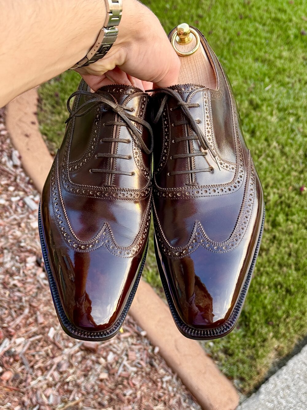 A person holds a pair of polished brown dress shoes with brogue detailing, featured in the context of the Americas Shoe Shining Championships.