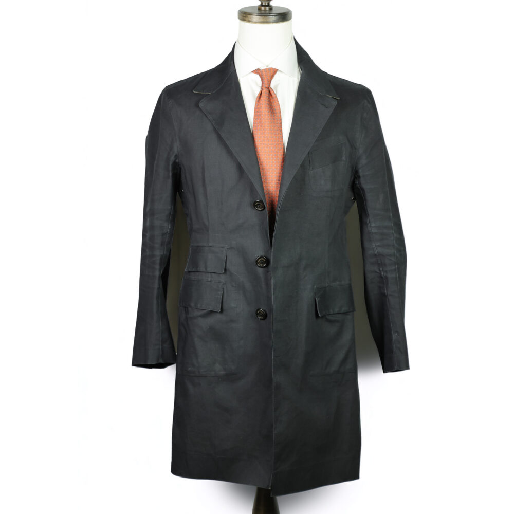 A dark gray overcoat displayed on a mannequin, paired with a light-colored shirt and an orange tie.