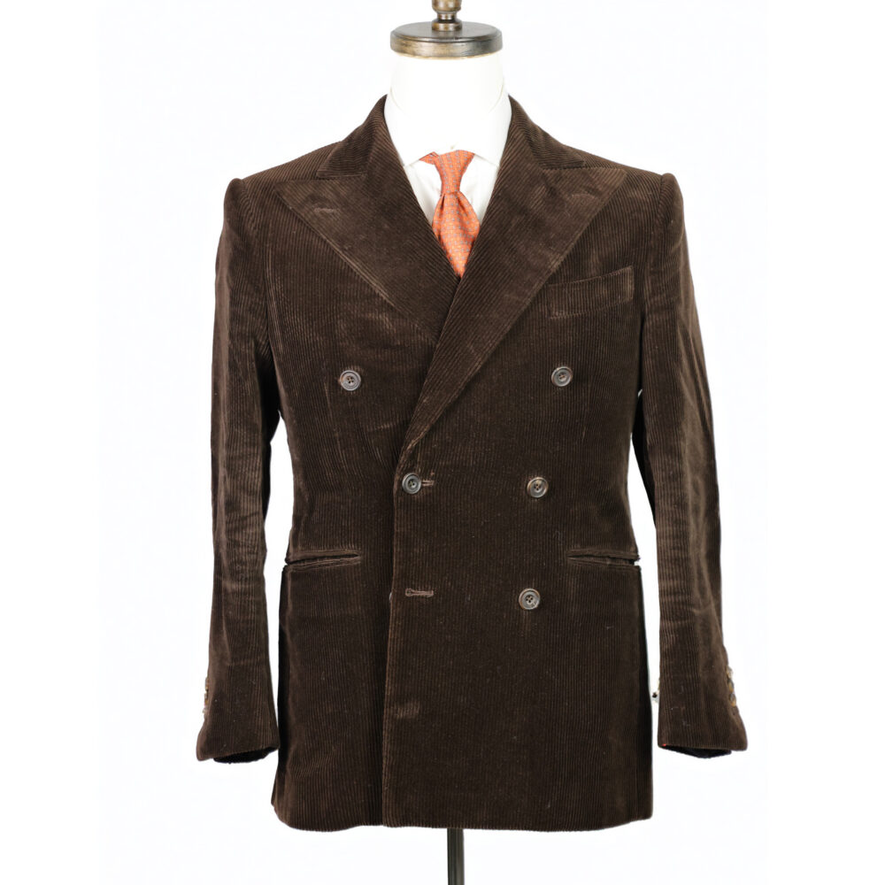A brown corduroy double-breasted jacket displayed on a mannequin, paired with a white shirt and orange tie.