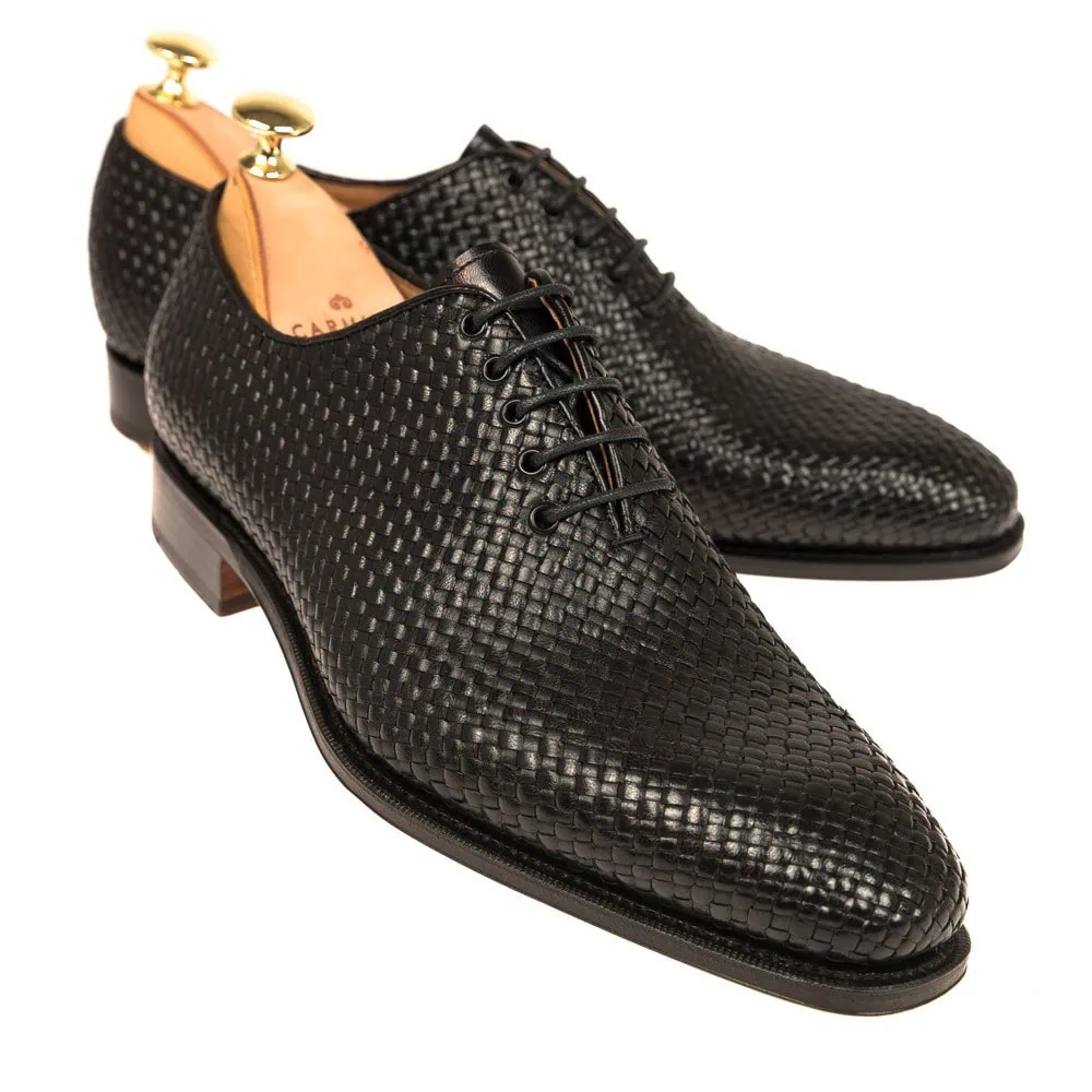 A pair of black woven leather dress shoes with laces and wooden shoe trees.