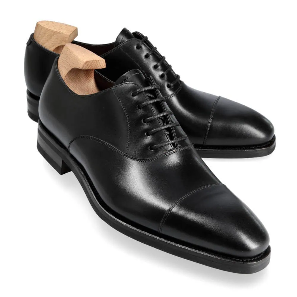 A pair of black leather dress shoes with a polished finish and wooden shoe trees.