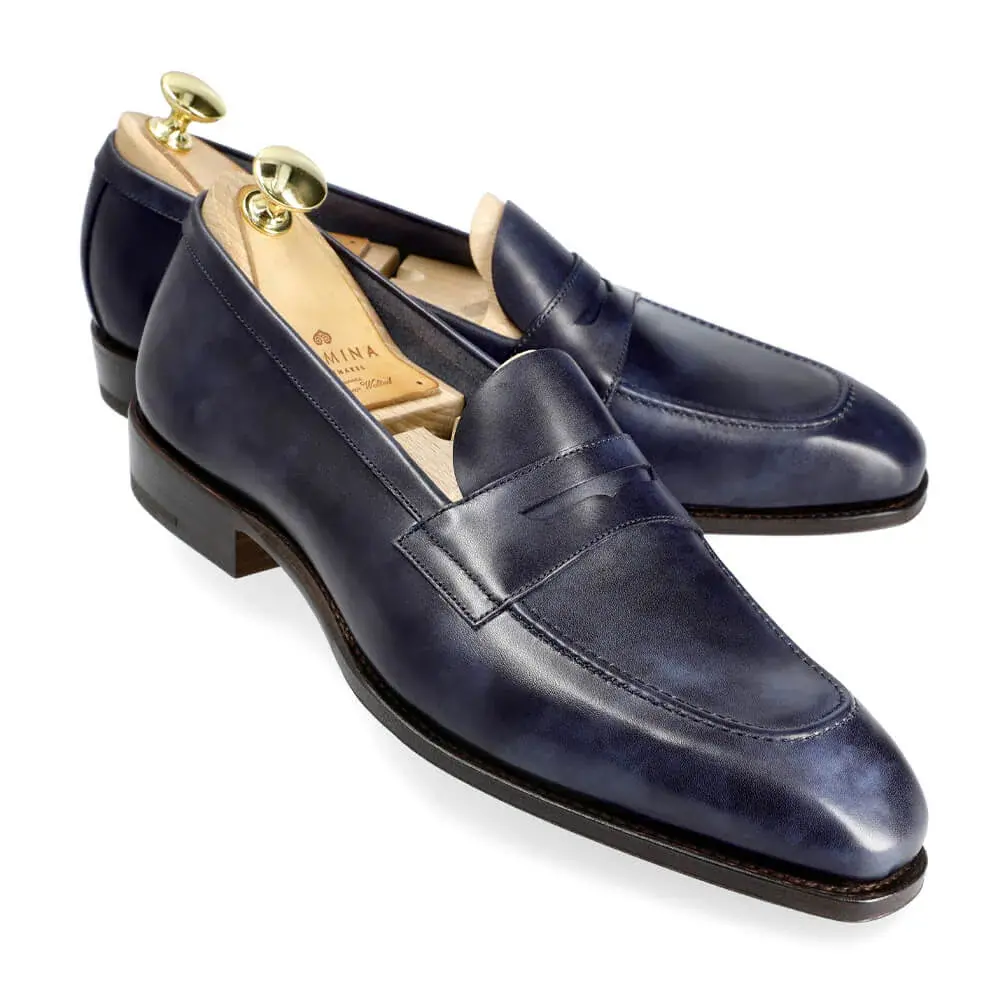 Navy blue leather loafers with a sleek design and gold shoehorns.