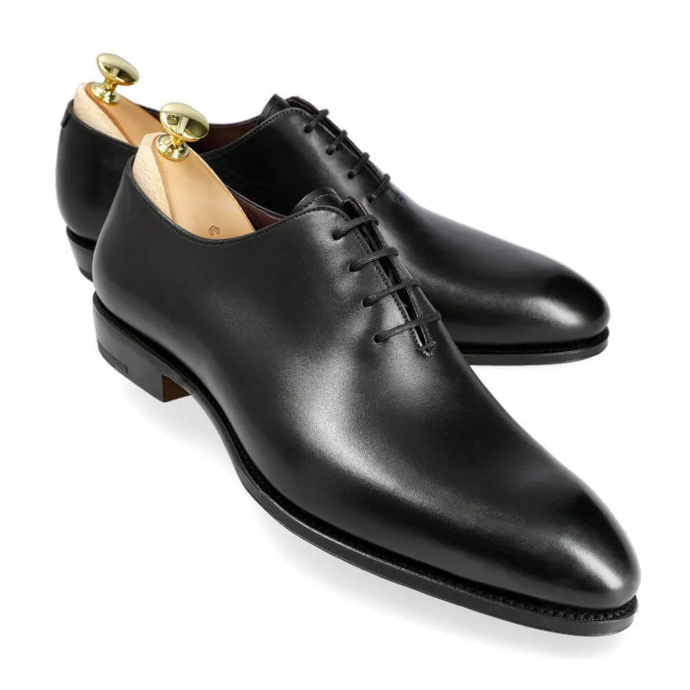 A pair of elegant black leather dress shoes with laces and gold shoe trees.