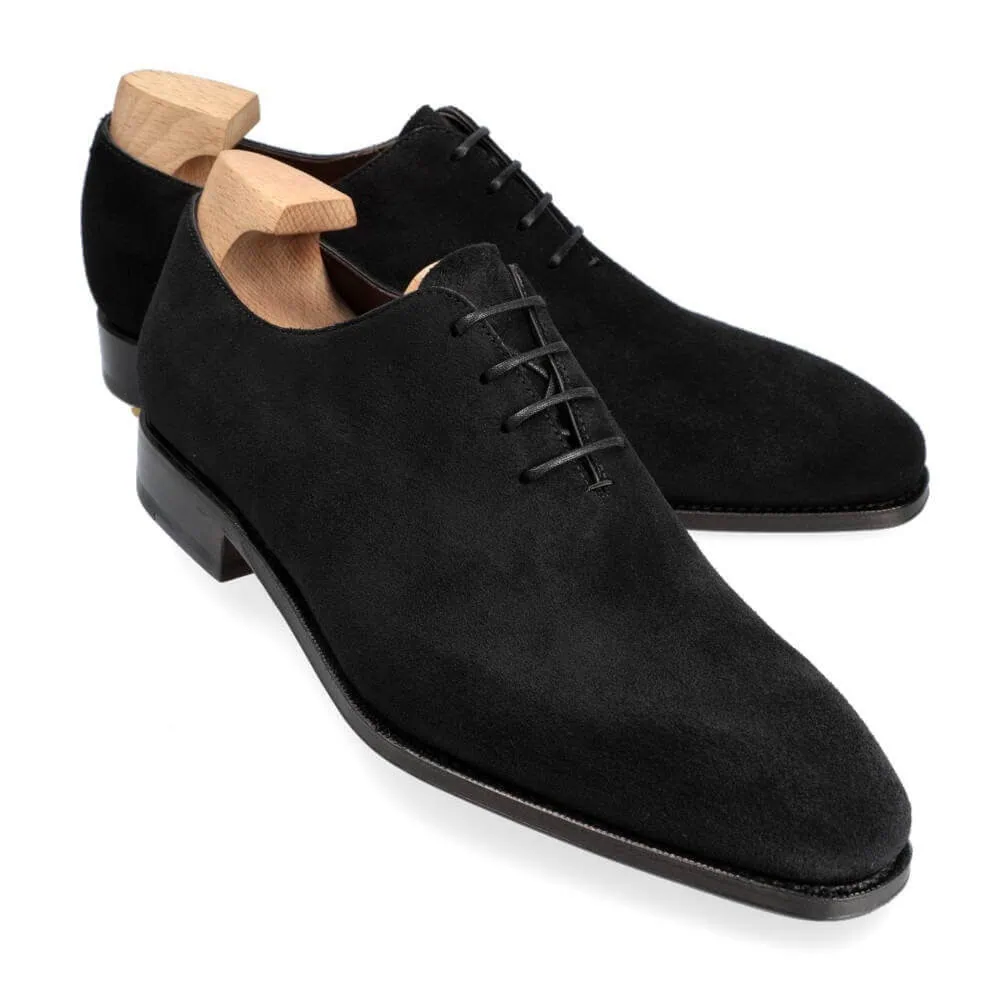 A pair of black suede dress shoes with wooden shoe trees inserted.