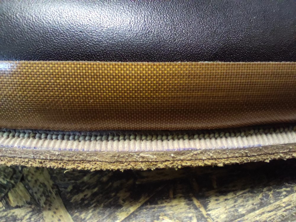 Close-up of a shoe sole featuring black leather, a brown textured layer, and visible stitching along the edge.
