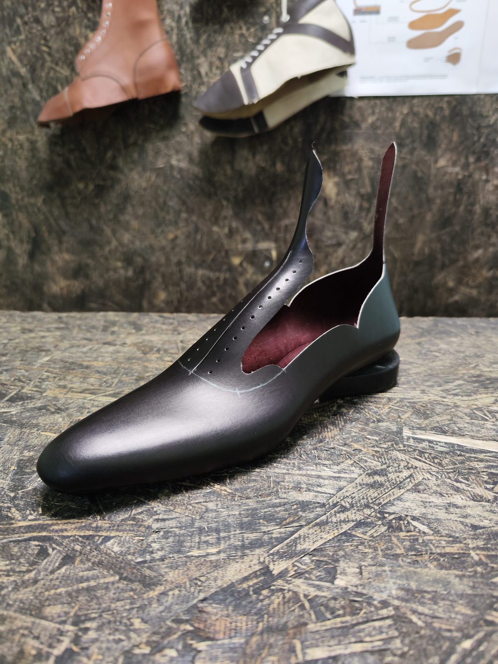 A sleek black shoe with a rounded toe and cut-out sides, featuring a maroon interior.