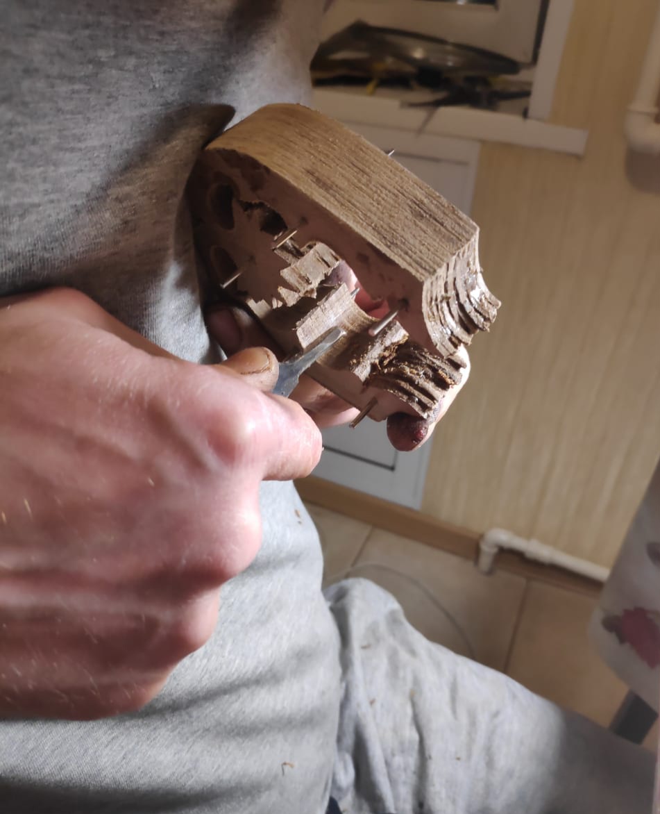 A person carves a wooden shoe last with a knife, showcasing intricate details in the wood.