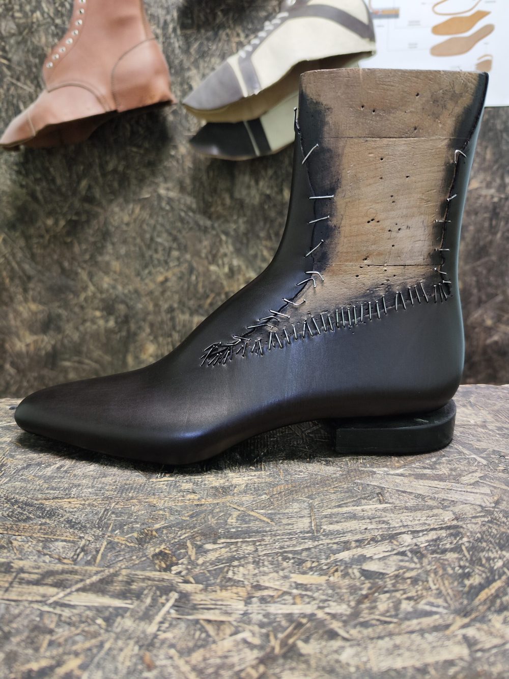 A sleek black leather boot with visible stitching details and a wooden sole.