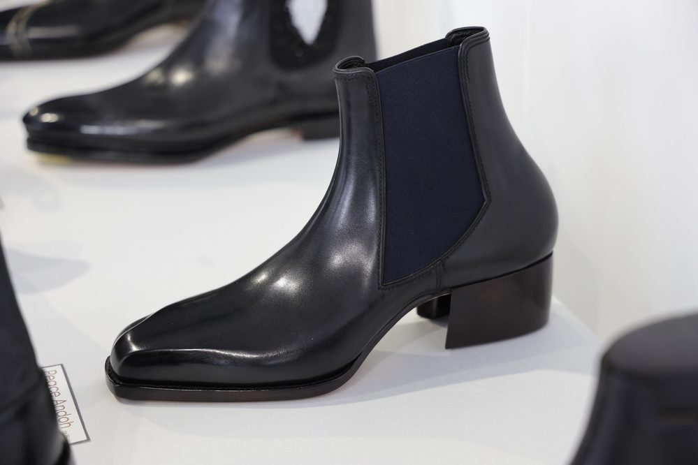 A sleek black leather Chelsea boot with a navy elastic side panel and a wooden heel.