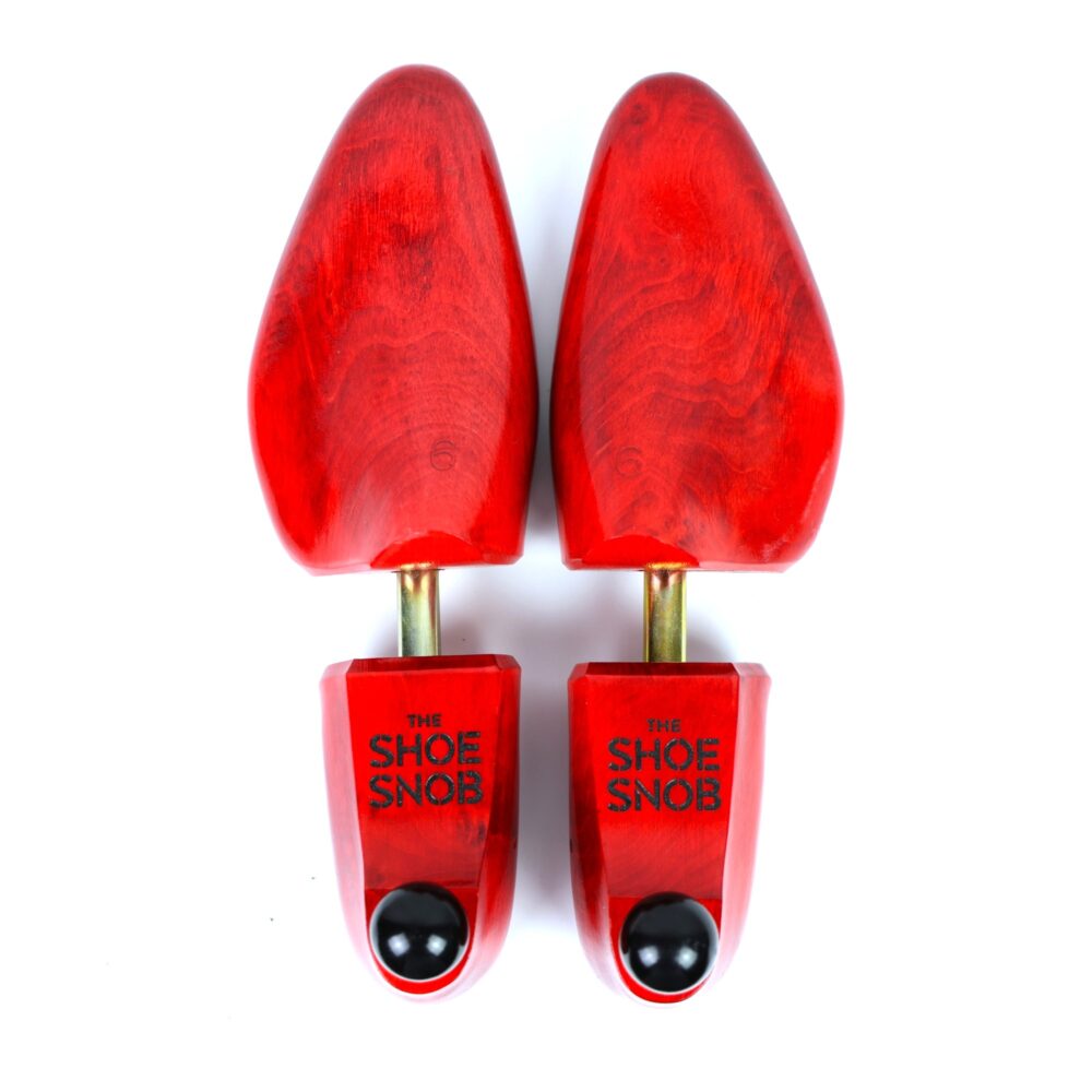 A pair of red wooden shoe trees with gold metal rods and black knobs, labeled "THE SHOE SNOB."