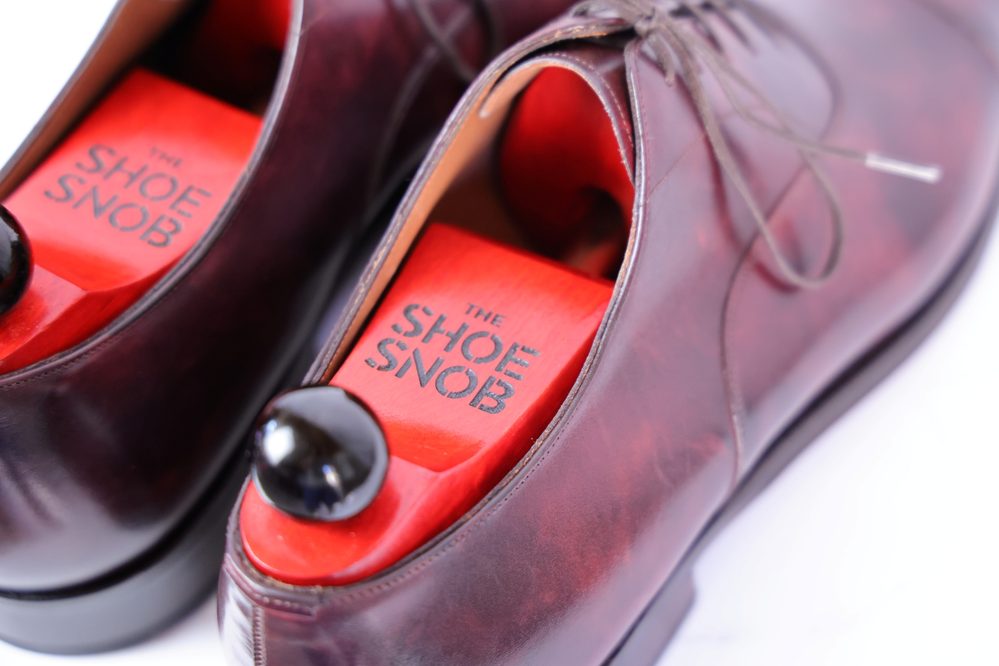 A close-up of a pair of burgundy shoes featuring The Shoe Snob's Lightweight Shoe Trees in red wood with a black knob.
