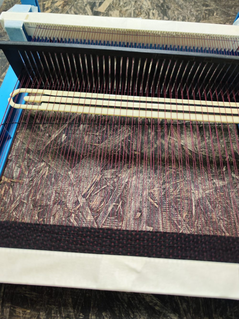 A weaving loom with purple and black threads is shown, featuring two white shuttles.