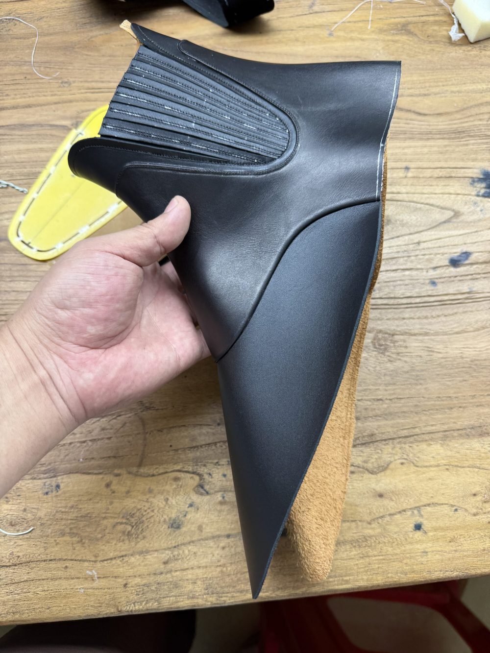 A hand holds a sleek black shoe upper made of leather with a textured design along the top edge.
