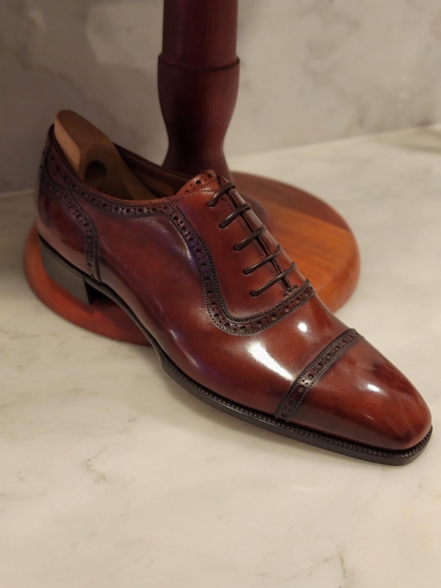 A polished brown leather dress shoe with decorative perforations and a cap toe.
