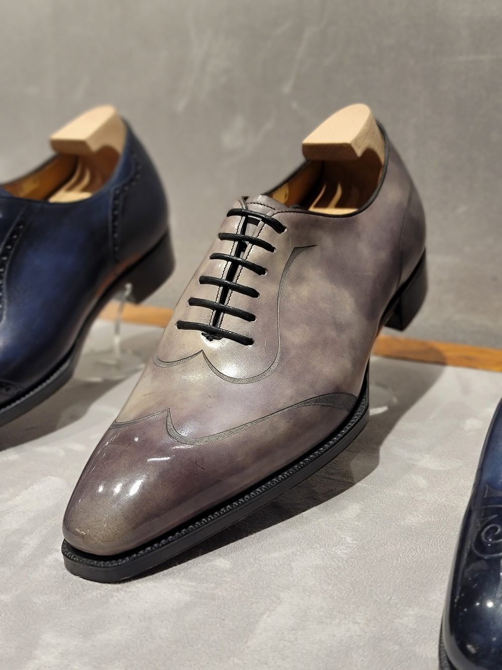 A gray and black leather dress shoe with decorative stitching and laces.