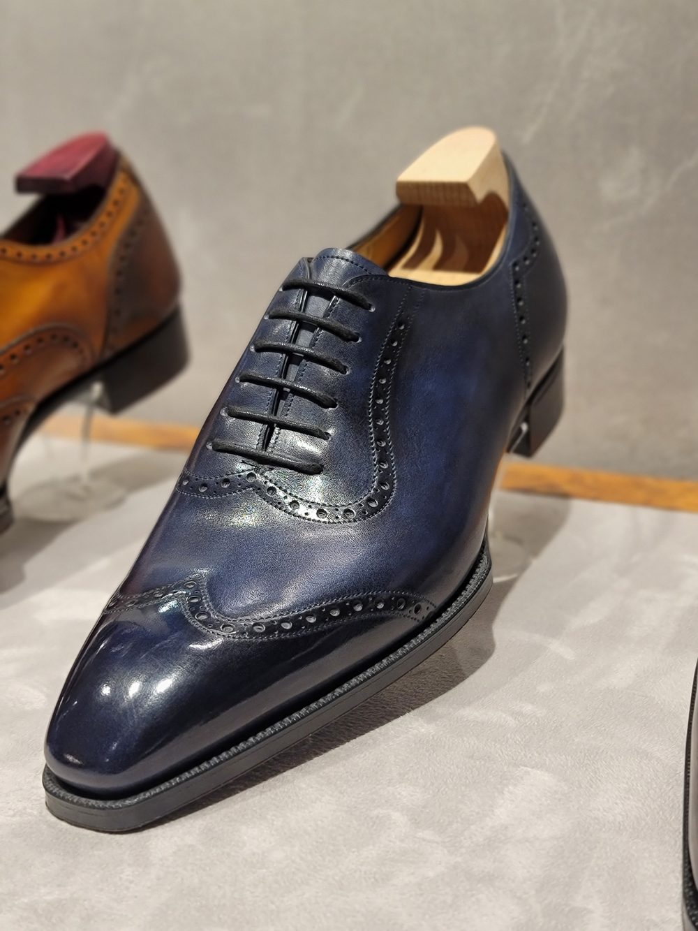 A polished navy leather dress shoe with brogue detailing and a wooden shoe tree.