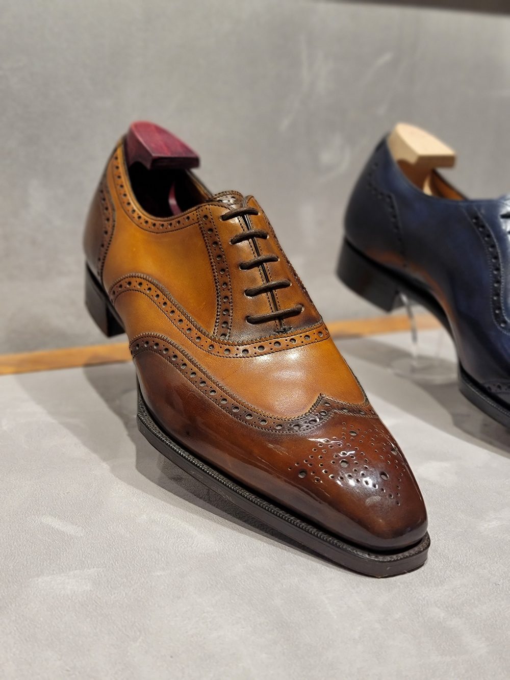 A brown leather dress shoe with brogue detailing and a pointed toe.