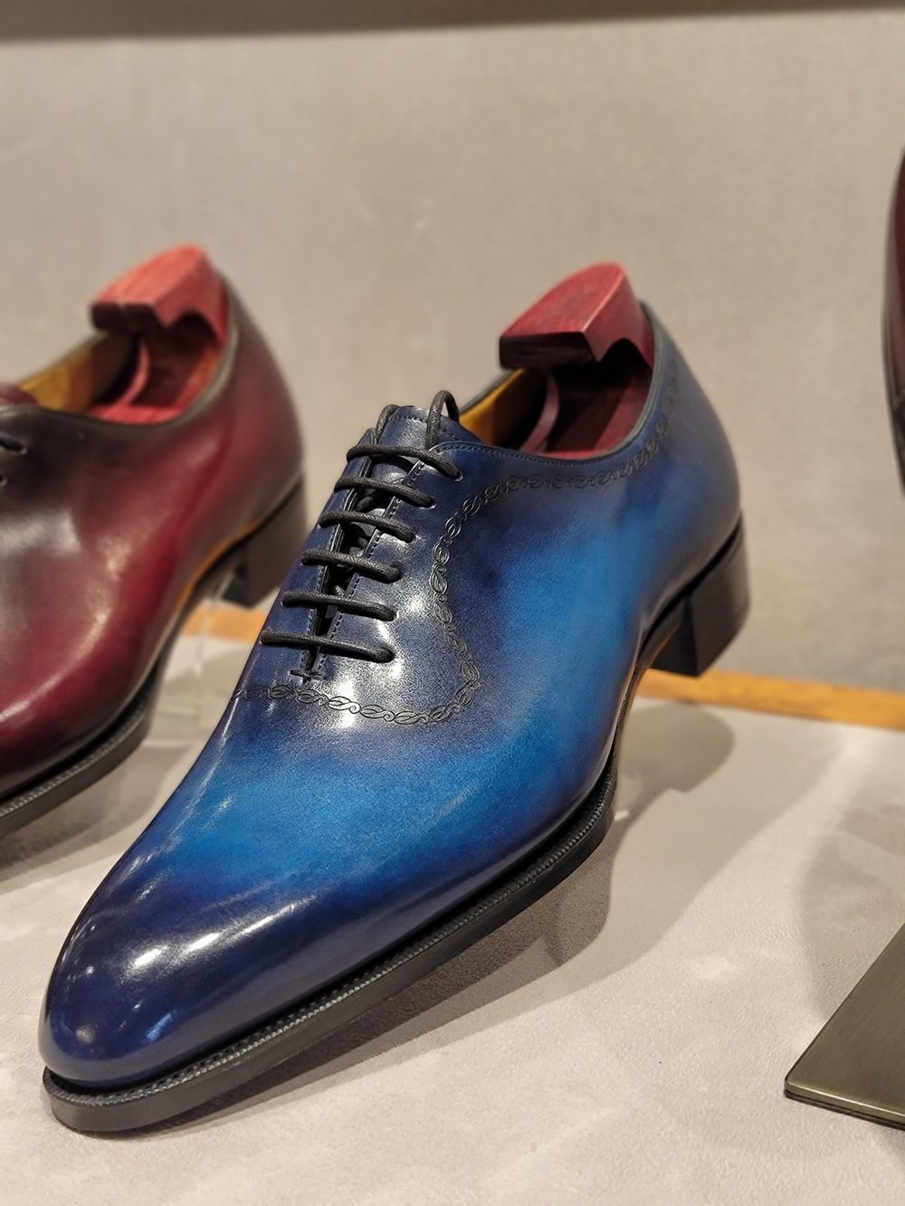 A polished blue leather shoe with a lace-up design, displayed alongside a burgundy shoe.