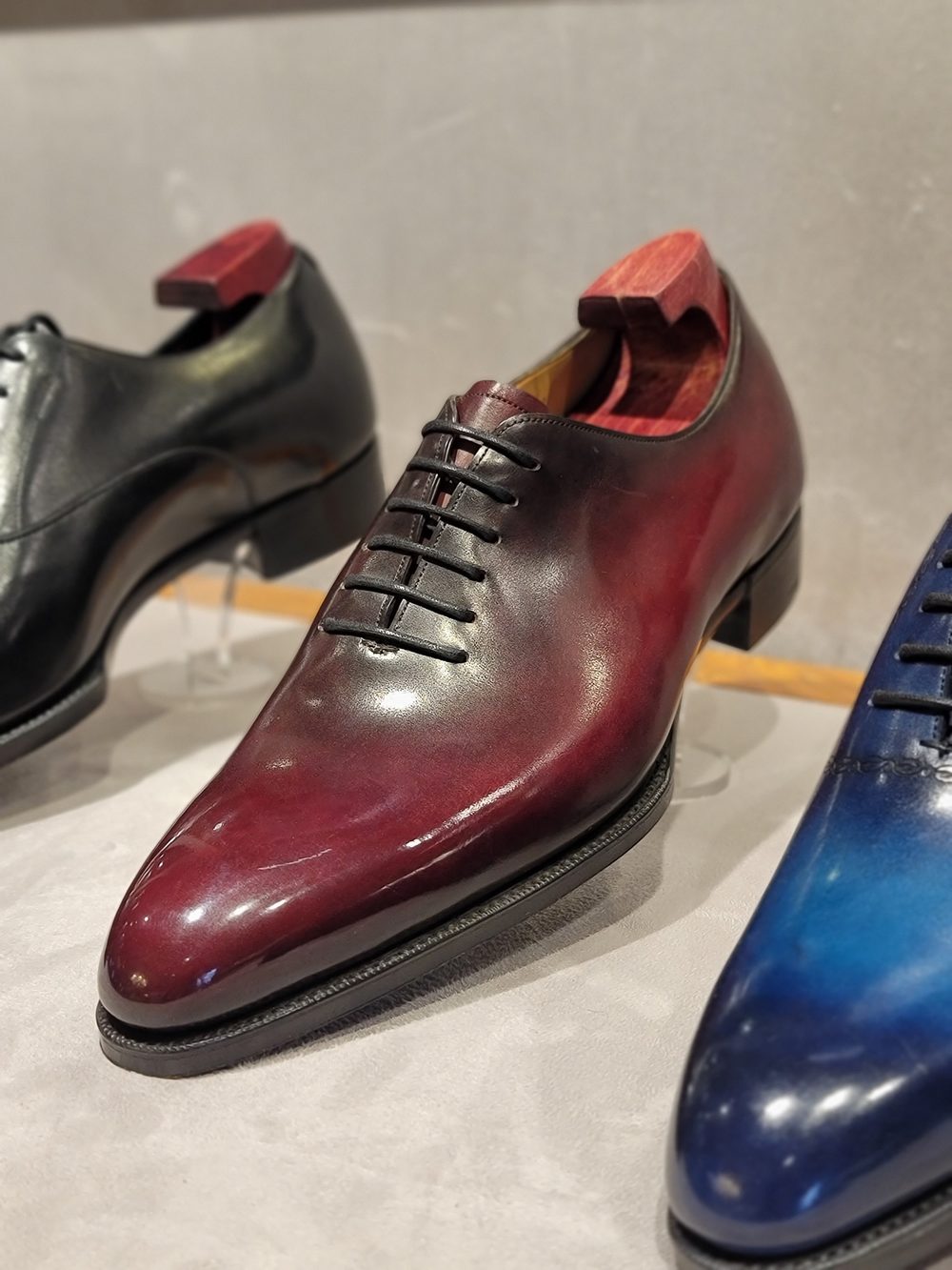 A polished burgundy leather shoe with a pointed toe and black laces, displayed alongside a black shoe.