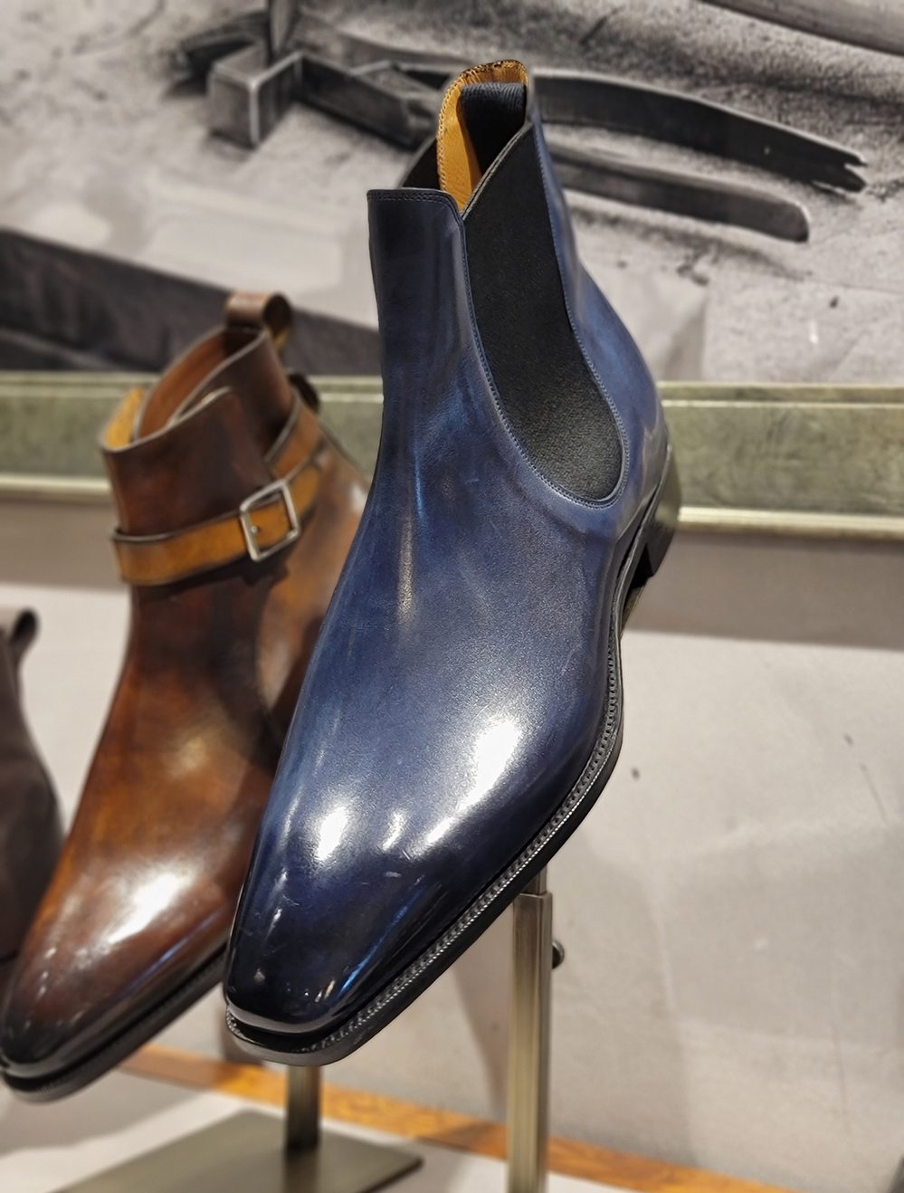 A polished blue leather Chelsea boot displayed on a stand.