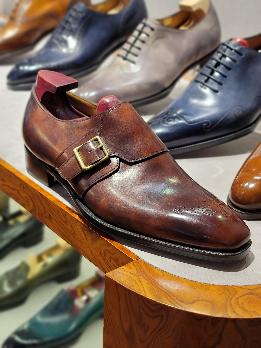 A polished brown leather shoe with a buckle sits prominently in the foreground, showcasing its elegant design.