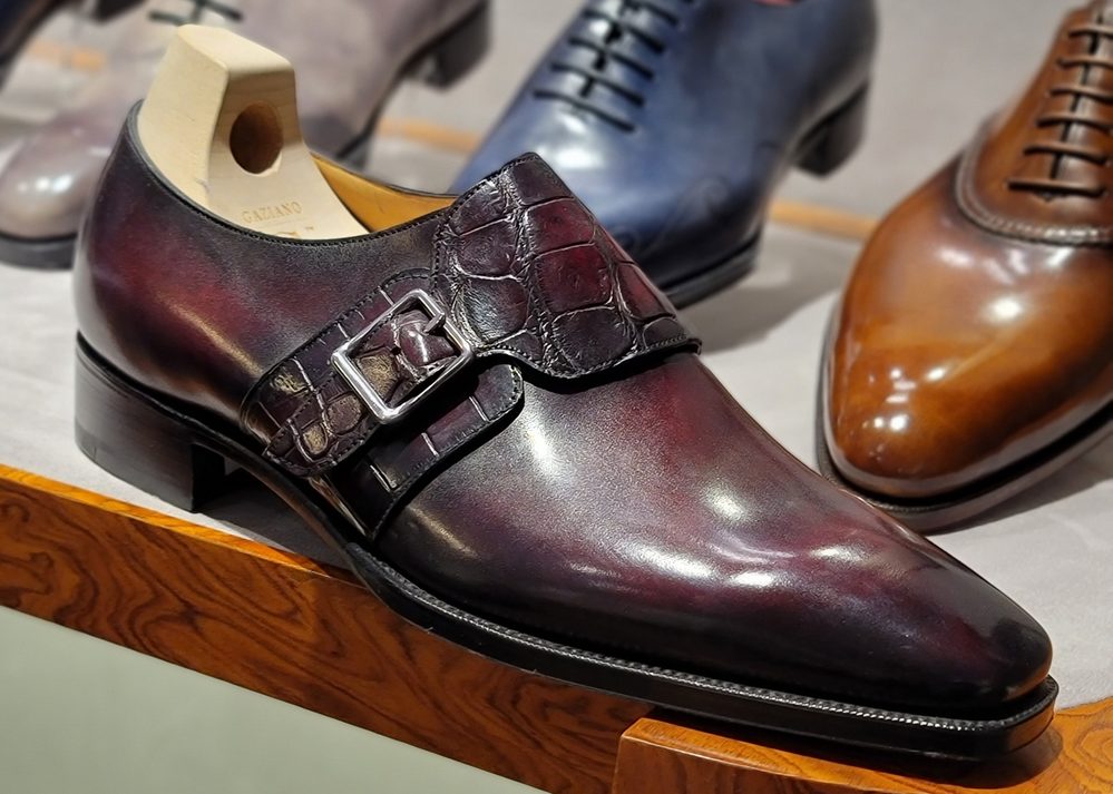 A polished burgundy leather shoe with a crocodile leather strap and silver buckle.