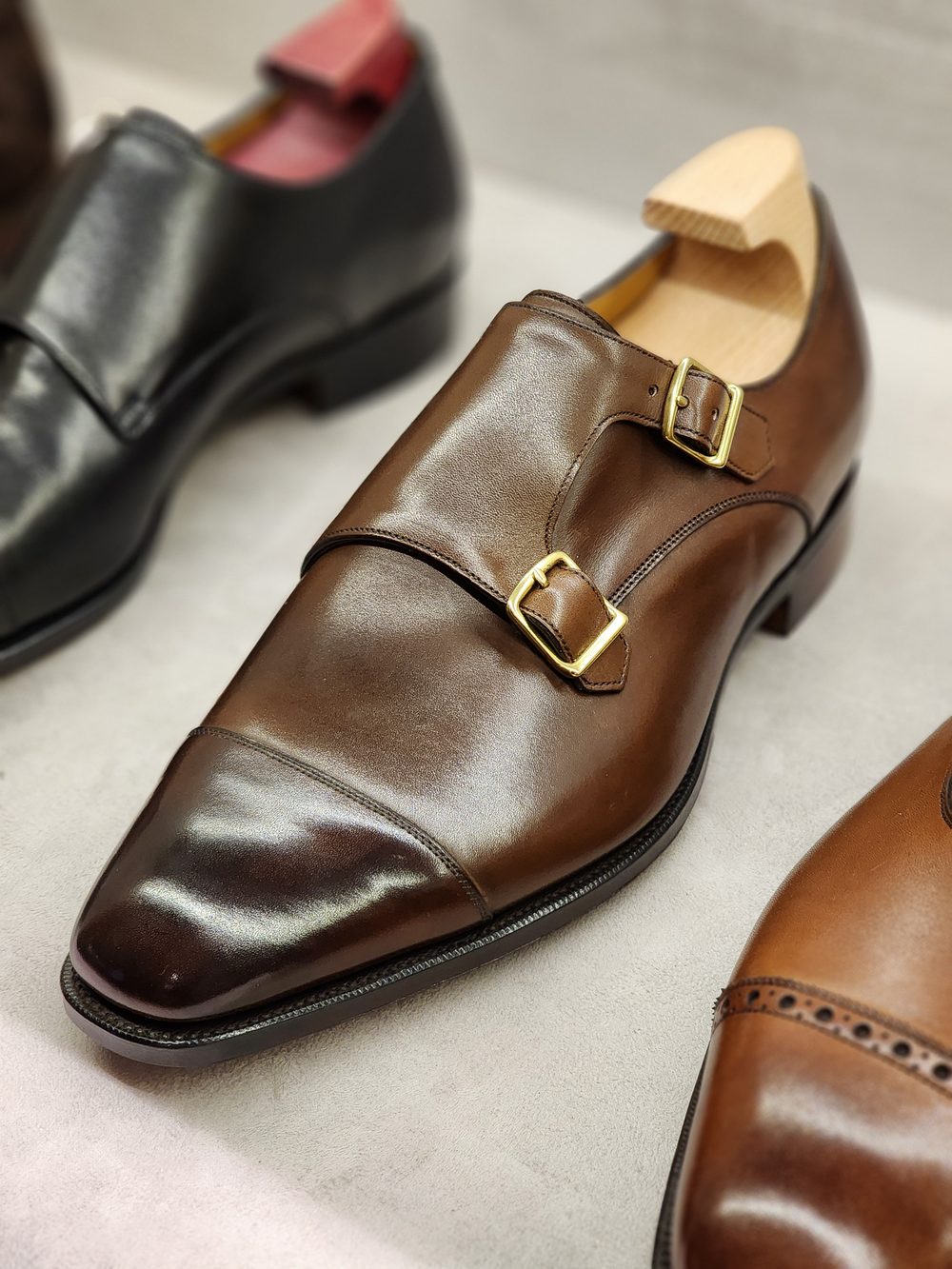 A polished brown leather shoe with double buckles and a wooden shoe tree.