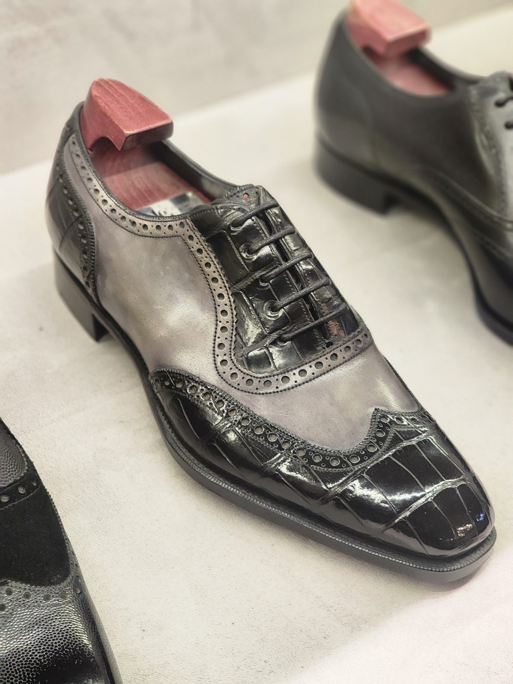 A black and grey leather dress shoe with decorative brogue detailing and a wooden shoe tree inserted.
