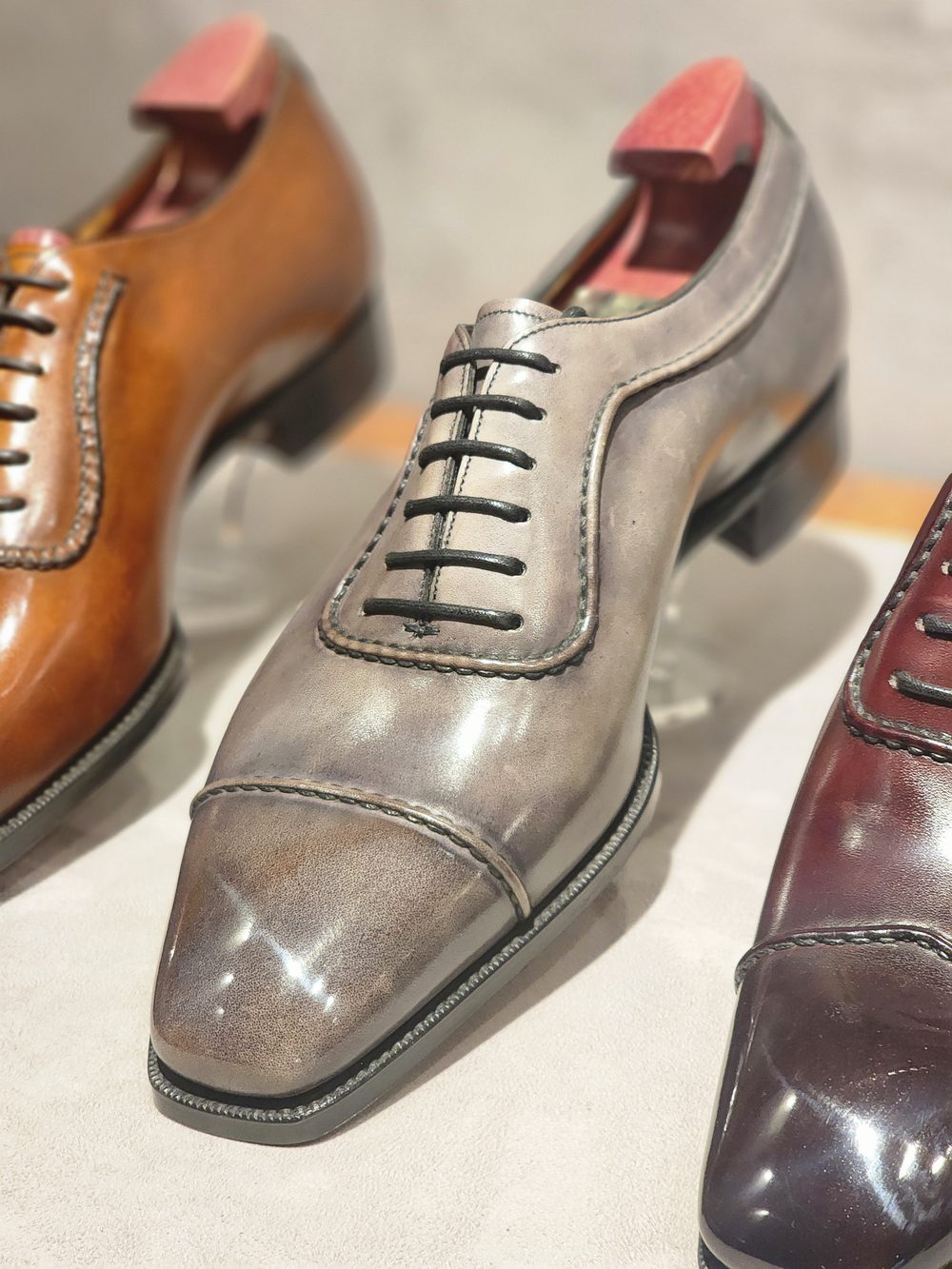 A polished gray dress shoe with black laces is featured prominently, alongside a brown shoe and a dark red shoe.