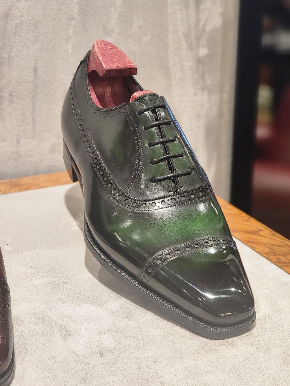 A polished black leather shoe with a pointed toe and decorative brogue detailing.
