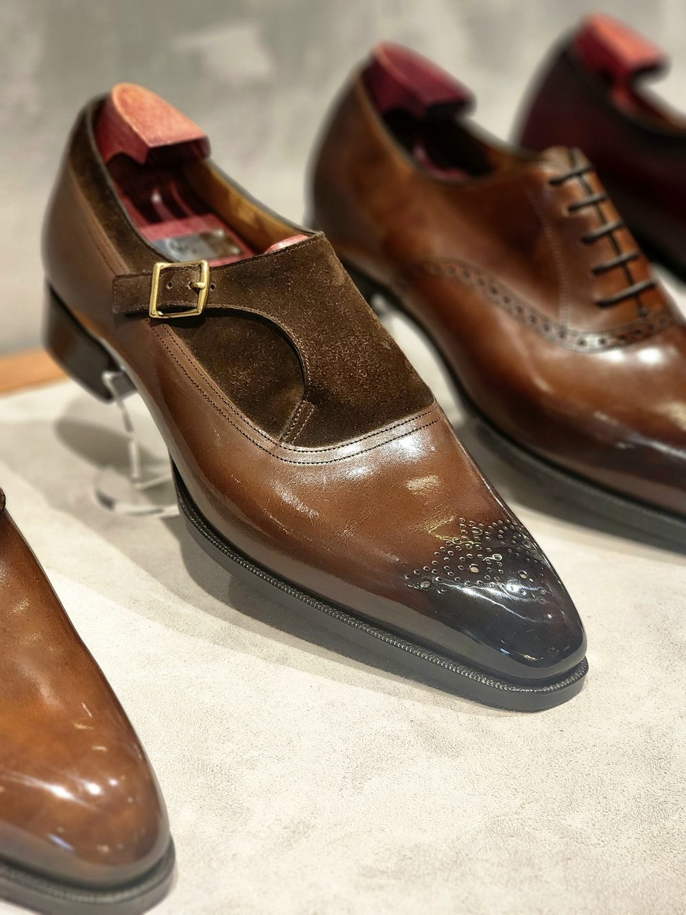 A pair of brown leather dress shoes, featuring a suede strap with a gold buckle and a polished black toe.